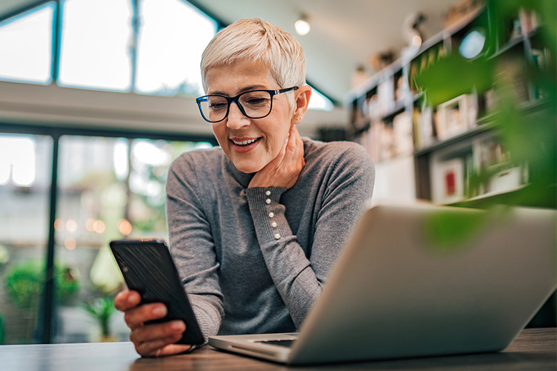 Woman using phone and laptop at home office